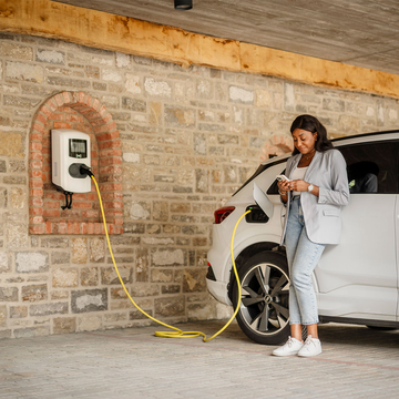 Frau lehnt an E-Auto an Ladestation